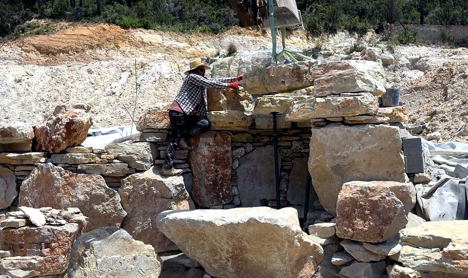 Joel McEwen Patterson setting the main waterfall keystone by hand, guided by excavator — Lisbon Natural Pool Oasis